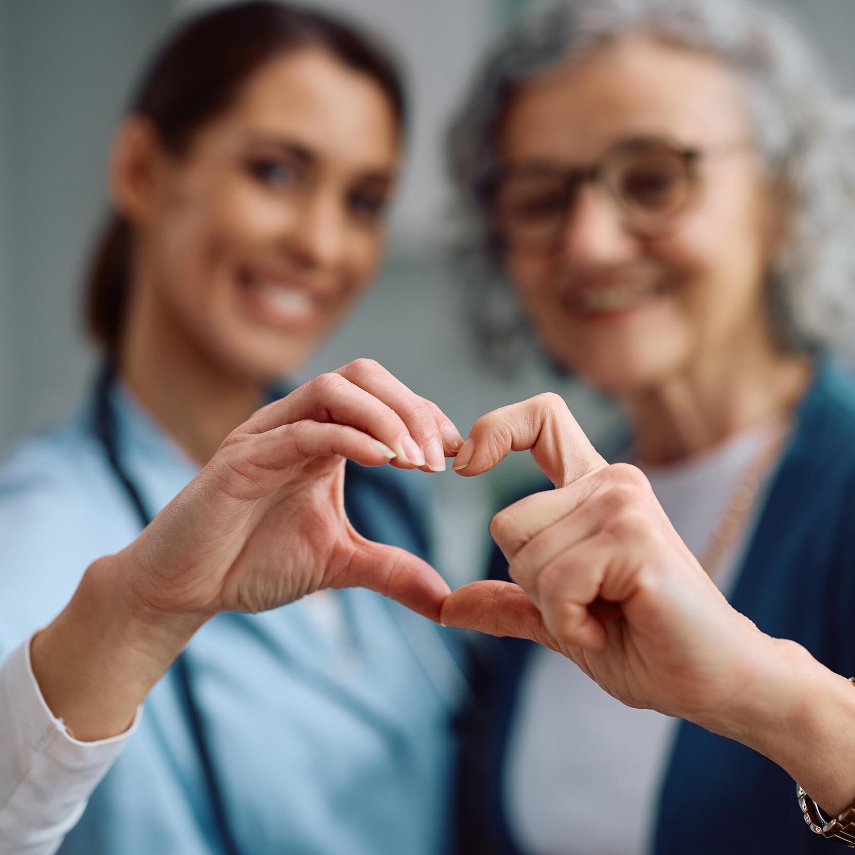 Close up of nurse and senior woman making heart shape with hands during home visit.
